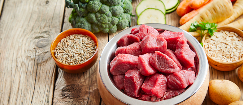 Rohes Fleisch, Gemüse und Getreide zum Barfen von Katzen liegen auf einer Holzplatte.