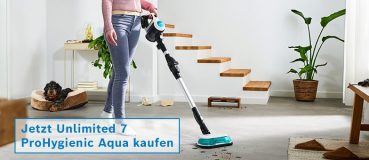 Eine Person saugt mit dem Unlimited 7 Pro Hygienic Aqua, im Hintergrund ein Hund in einem Körbchen. 